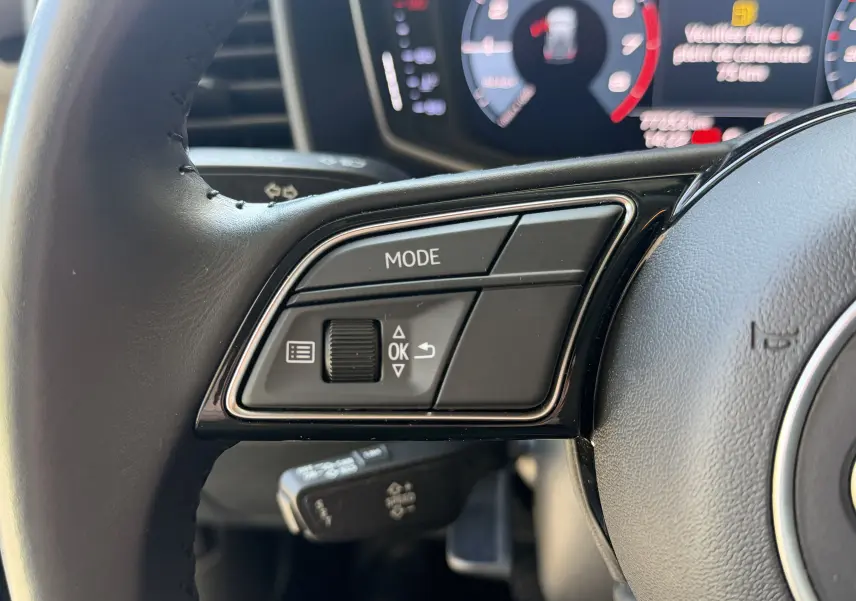 Gros plan sur les commandes gauche du volant noir de l’Audi A1 Sportback 2020, avec affichage numérique en arrière-plan.