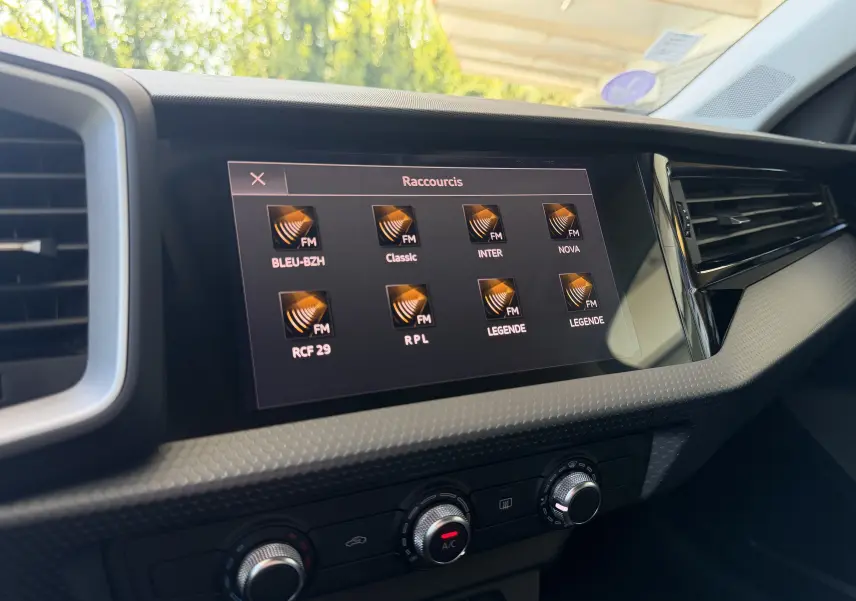 Écran tactile central de l’Audi A1 Sportback 2020 affichant les stations radio FM, avec commandes de climatisation en dessous.