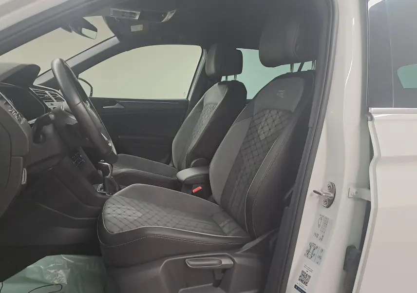 Intérieur côté gauche du Volkswagen Tiguan 1.4 eHybrid 245 DSG6 R-LINE 2023 avec sièges noirs en tissu et cuir, porte blanche ouverte.