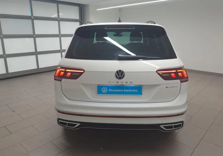 Vue arrière d'un Volkswagen Tiguan blanc pur 2023 hybride rechargeable avec feux allumés et badge eHybrid visible.