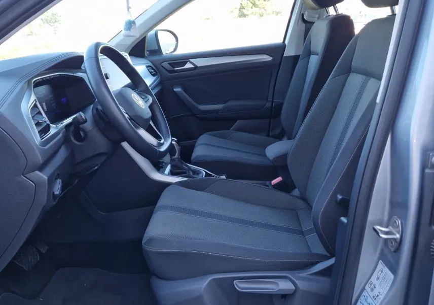 Intérieur côté conducteur d'un Volkswagen T-Roc gris pyrite 2023, sièges tissu noirs et tableau de bord moderne.