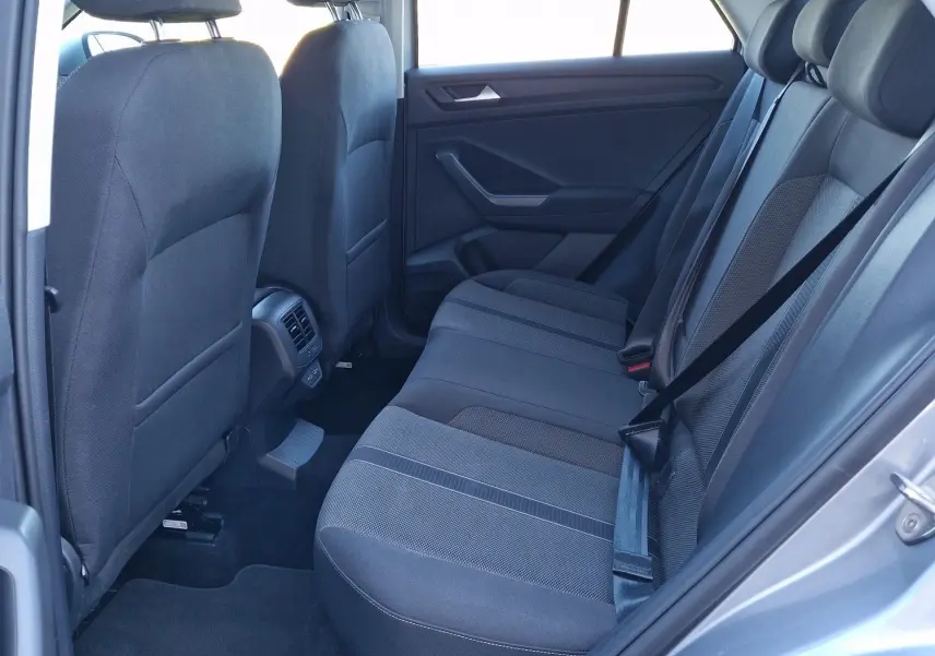 Vue côté gauche de l'habitacle arrière du Volkswagen T-Roc gris pyrite 2023 avec sièges tissu noirs et ceinture attachée.