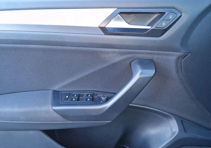 Gros plan sur la porte côté gauche du Volkswagen T-Roc gris Pyrite, montrant les commandes des vitres et la poignée intérieure.