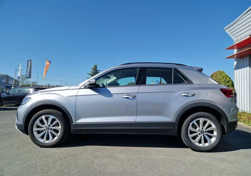 Profil côté gauche d'un Volkswagen T-Roc gris pyrite 2023, soulignant ses lignes modernes et ses jantes alliage.