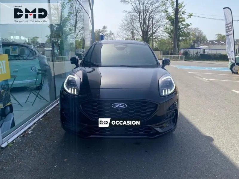Vue frontale d'un Ford Puma noir Agate Métallisée avec phares LED allumés, garé devant une vitrine.