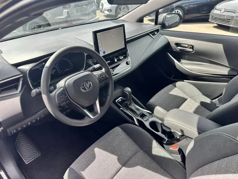 Intérieur avant droit de la Toyota Corolla 2025 hybride noire, volant multifonction et écran tactile central visible.