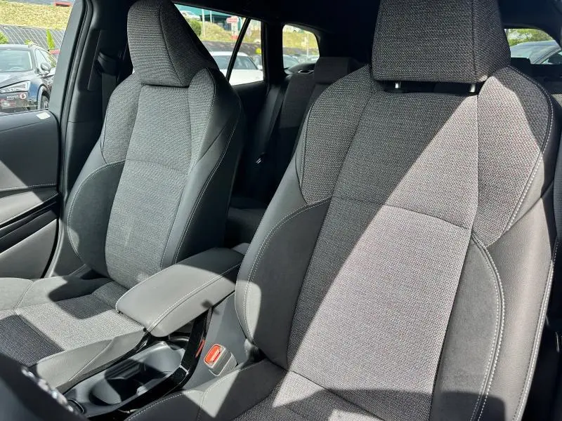 Gros plan sur les sièges avant en tissu noir et alcantara de la Toyota Corolla 1.8 Hybrid 2025, avec accoudoir central.