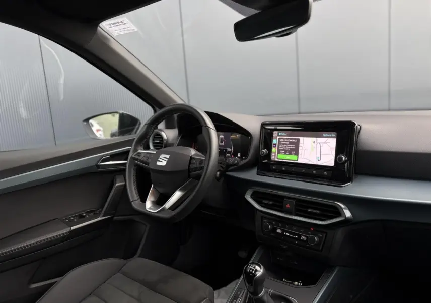 Vue intérieure côté conducteur du tableau de bord du SEAT Arona TSI 115 Xpérience avec écran tactile et volant cuir noir.