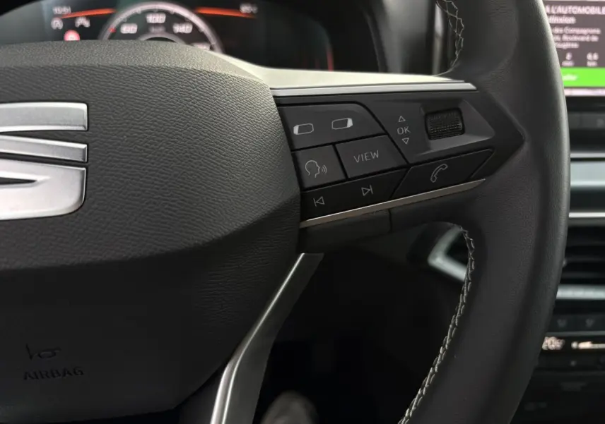 Gros plan sur le volant cuir multifonction du SEAT Arona TSI 115 Xpérience, avec commandes intégrées et logo SEAT visible.