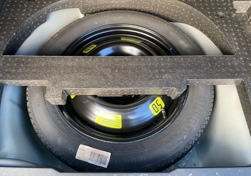 Roue de secours noire avec étiquette jaune, logée dans le coffre d’un Peugeot 2008 gris platinium de 2019.