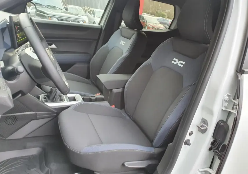 Vue intérieure côté conducteur du Dacia Duster blanc glacier 2025, sièges tissu avec logo distinctif DC brodé.