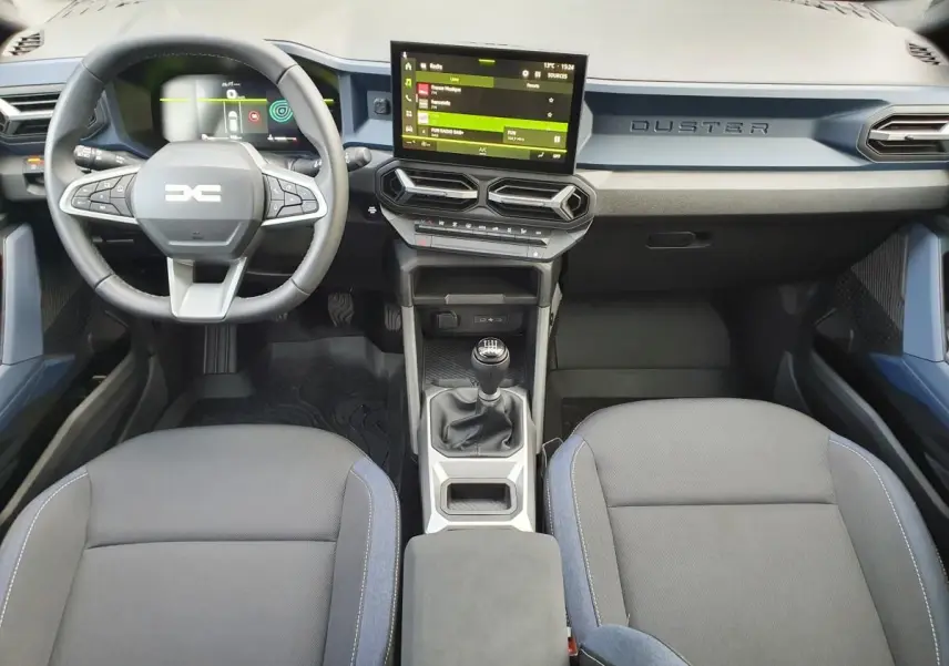 Vue intérieure avant du Dacia Duster 2025 avec tableau de bord moderne, écran tactile, volant multifonction et boîte manuelle.