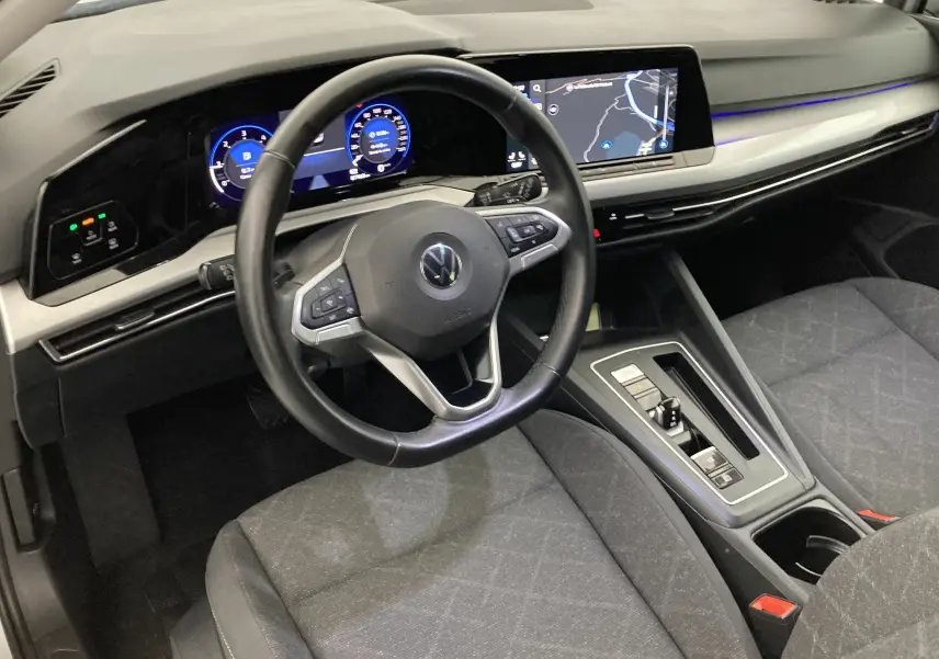 Vue intérieure de face du poste de conduite d'une Volkswagen Golf VIII gris reflex, avec tableau de bord digital et écran central tactile.
