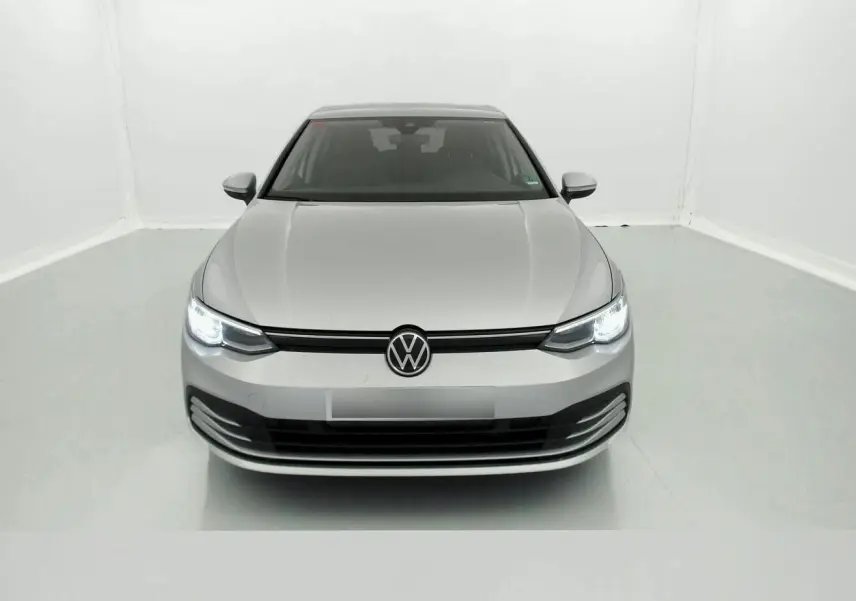 Vue frontale d'une Volkswagen Golf VIII gris reflex avec phares allumés dans un studio blanc.