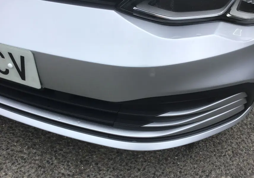Gros plan sur la partie avant basse gris reflex d'une Volkswagen Golf VIII avec calandre et plaque d'immatriculation partielle.