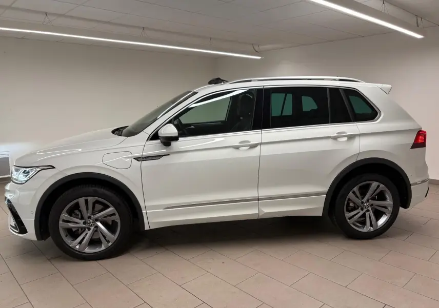 Profil droit d'un Volkswagen Tiguan blanc pur 2023 hybride rechargeable avec jantes R-Line distinctives en intérieur neutre.