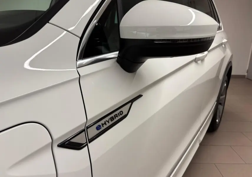 Gros plan sur le côté gauche blanc pur du Volkswagen Tiguan 1.4 eHybrid 2023 avec logo eHybrid et rétroviseur.