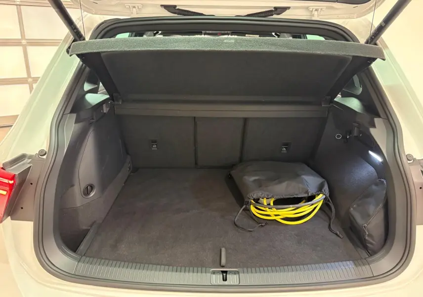 Coffre ouvert d'un Volkswagen Tiguan blanc pur 2023, version hybride rechargeable, avec câble de recharge visible.