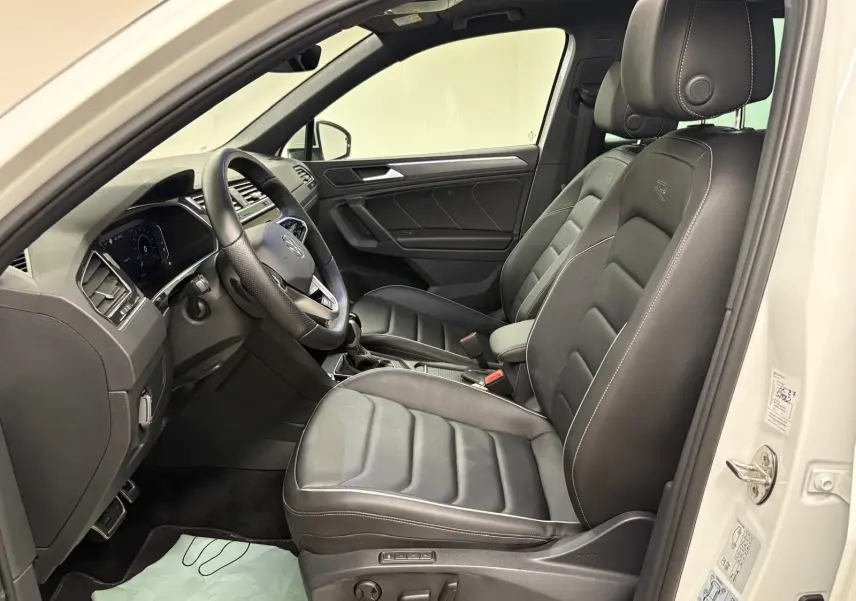 Vue intérieure côté conducteur du Volkswagen Tiguan blanc pur 2023, sièges en cuir noir R-Line exclusifs.