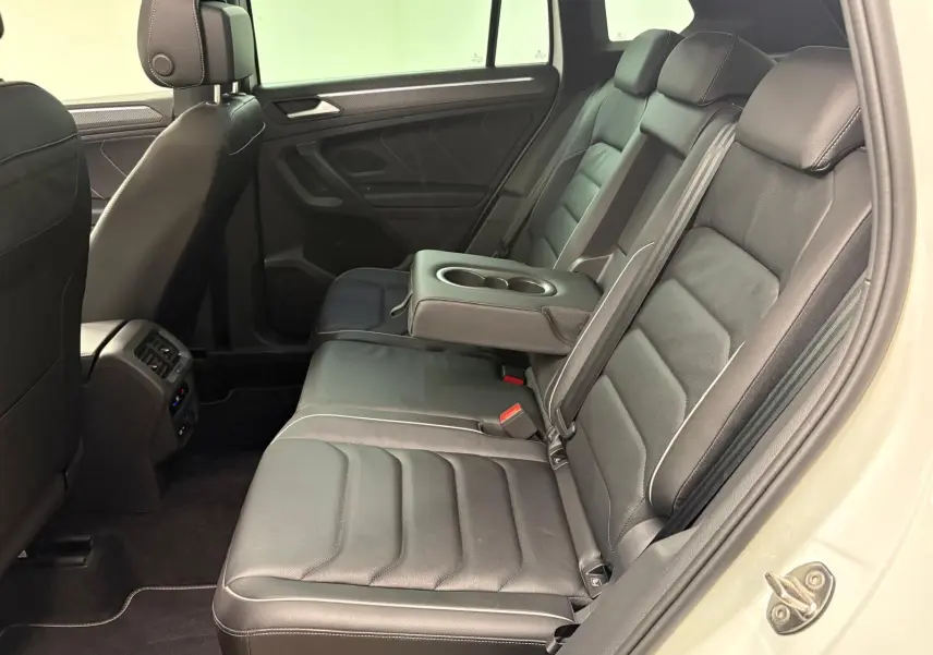 Vue intérieure côté droit des sièges arrière noirs en cuir du Volkswagen Tiguan blanc pur 2023, avec accoudoir central relevé.