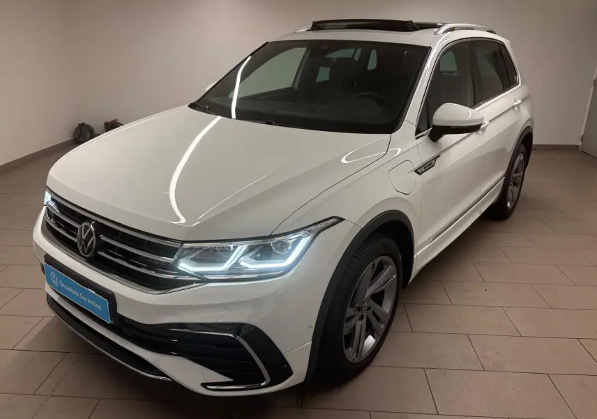 Volkswagen Tiguan blanc pur 2023 en vue 3/4 avant droit avec phares allumés et badge hybride sur aile.