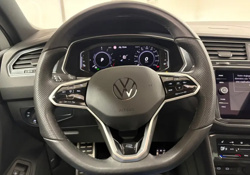 Vue rapprochée du volant noir perforé du Volkswagen Tiguan 1.4 eHybrid 2023 avec tableau de bord numérique allumé.