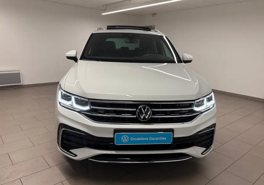 Vue frontale d'un Volkswagen Tiguan blanc pur 2023, version hybride rechargeable R-Line Exclusive avec phares LED allumés.