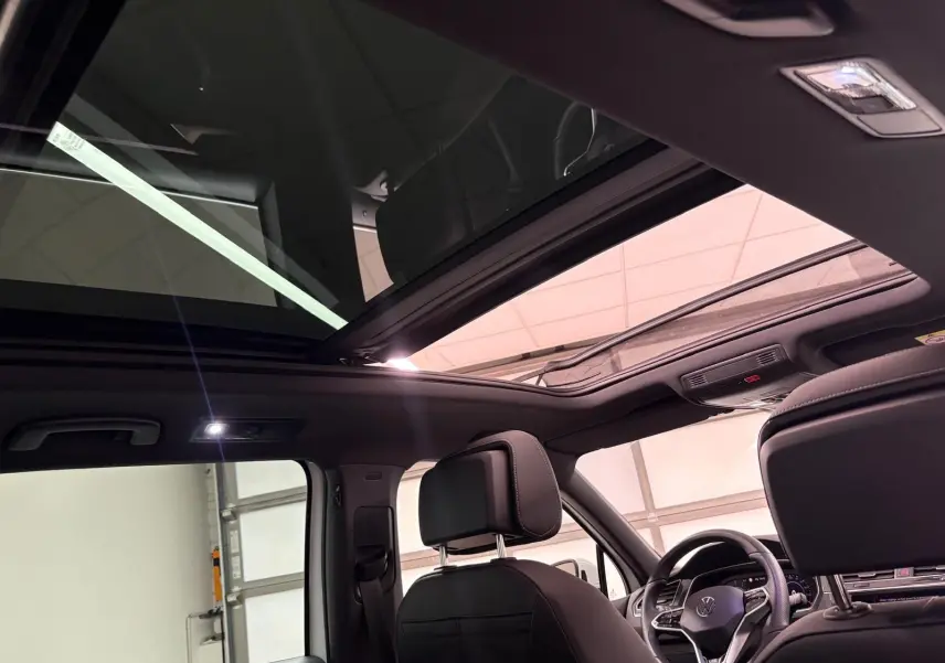 Toit panoramique ouvert et intérieur noir du Volkswagen Tiguan 1.4 eHybrid 2023 vu depuis l'arrière côté gauche.