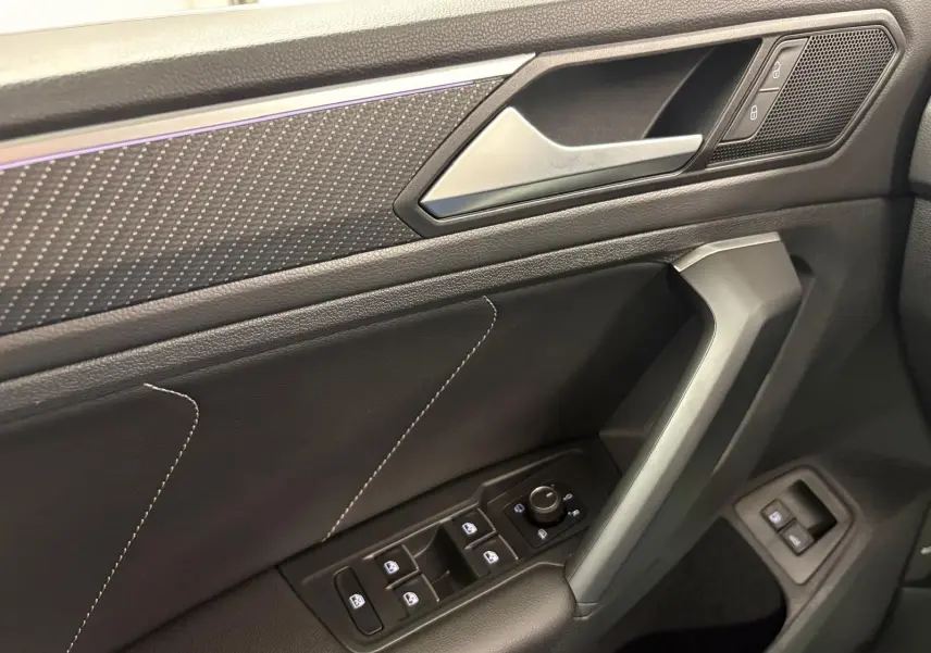 Gros plan sur la porte côté conducteur du Volkswagen Tiguan blanc pur 2023, avec commandes électriques et surpiqûres décoratives.