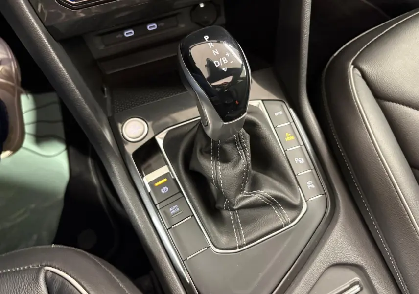 Le levier de vitesses automatique du Volkswagen Tiguan 2023 blanc pur, entouré de commandes de conduite et finition cuir noire.