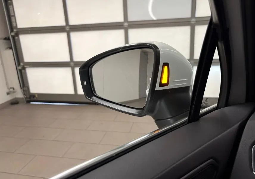 Rétroviseur extérieur côté gauche blanc pur du Volkswagen Tiguan 1.4 eHybrid 2023 avec clignotant allumé en intérieur de garage.