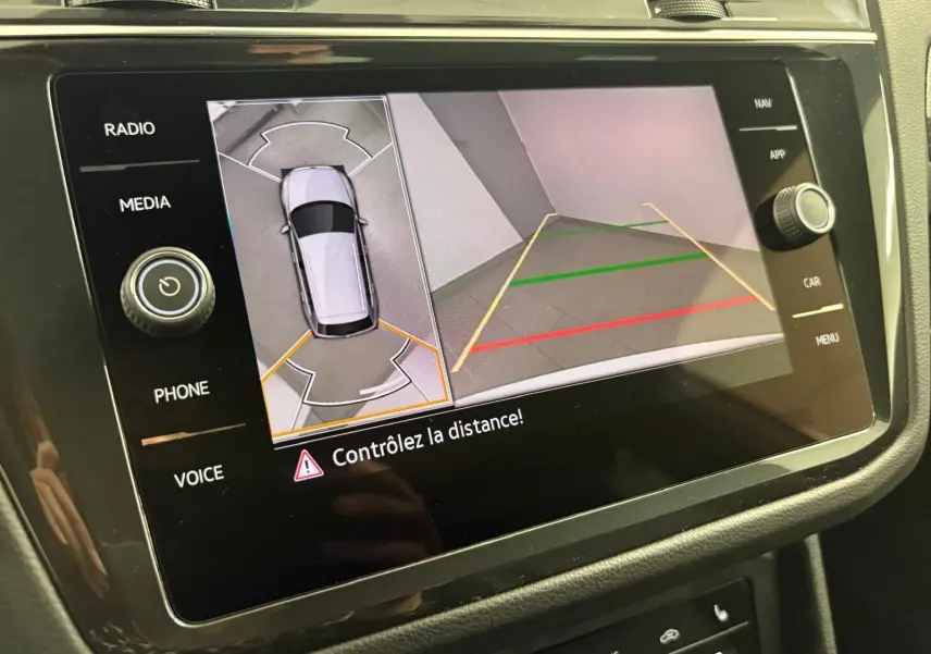 Écran multimédia du Volkswagen Tiguan 2023 blanc pur montrant la caméra de recul avec vue aérienne et lignes de guidage.