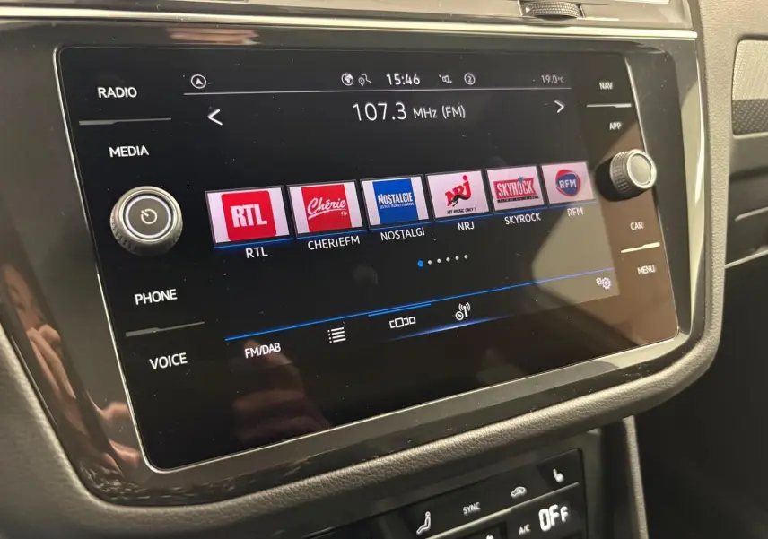 Écran tactile central du Volkswagen Tiguan 2023 blanc, affichant les stations radio FM avec commandes autour.