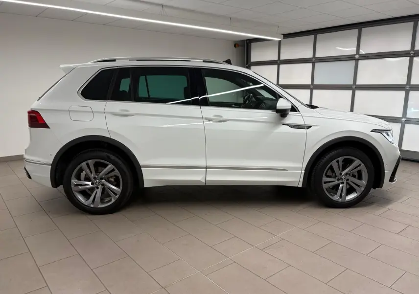 Profil côté gauche d'un Volkswagen Tiguan blanc pur 2023, version hybride rechargeable R-Line Exclusive en intérieur showroom.
