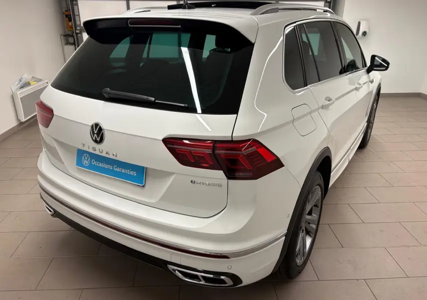Vue 3/4 arrière droite d'un Volkswagen Tiguan blanc pur hybride rechargeable avec finition R-Line Exclusive et feux LED distinctifs.