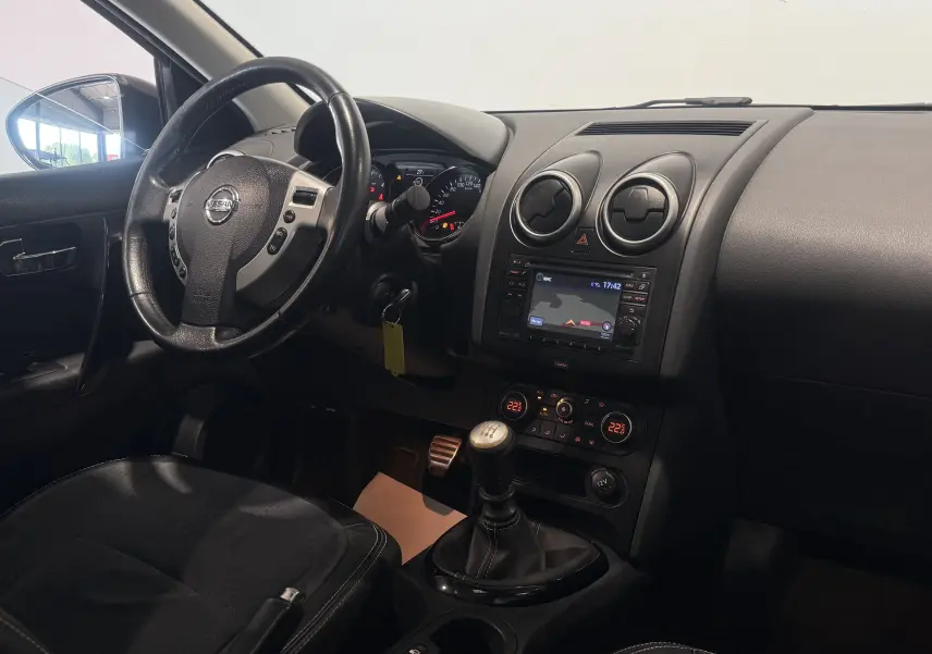 Intérieur du Nissan Qashqai+2 2014 en vue du poste de conduite, volant, tableau de bord et levier de vitesses manuelle visibles.