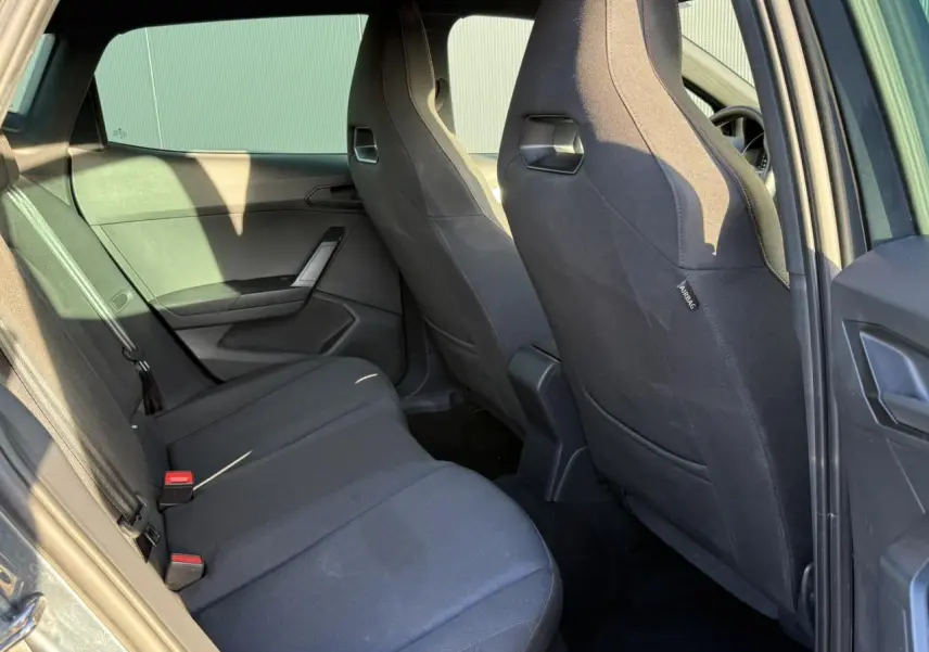 Vue intérieure arrière côté gauche de la SEAT IBIZA TSI 115 FR 2025 avec sièges tissu gris et ceintures noires.