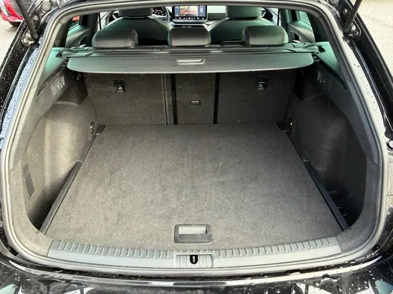 Coffre ouvert vu de l'arrière d'une SEAT LEON ST 1.5 eTSI Hybrid noir minuit métallisé avec cache-bagages et intérieur gris.