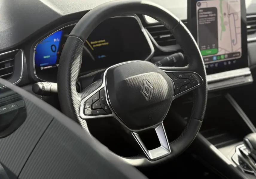 Vue rapprochée du volant noir perforé de la Renault SYMBIOZ avec écran numérique et console tactile visible en arrière-plan.