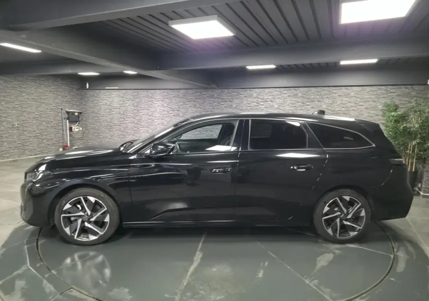 Peugeot 308 SW noire vue de profil côté gauche, jantes alliage 17'' et vitres surteintées en intérieur showroom.