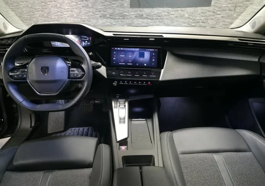 Vue intérieure avant de la Peugeot 308 SW 2024, tableau de bord noir avec écran tactile et volant cuir compact.