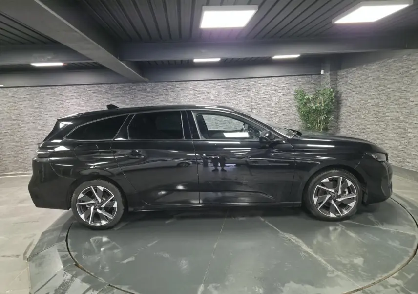 Peugeot 308 SW noire vue de profil côté gauche, avec jantes alliage 17'' et vitres surteintées en intérieur showroom.