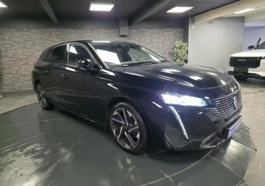 Peugeot 308 SW noire vue en 3/4 avant droit, avec feux LED allumés et jantes alliage 17 pouces.