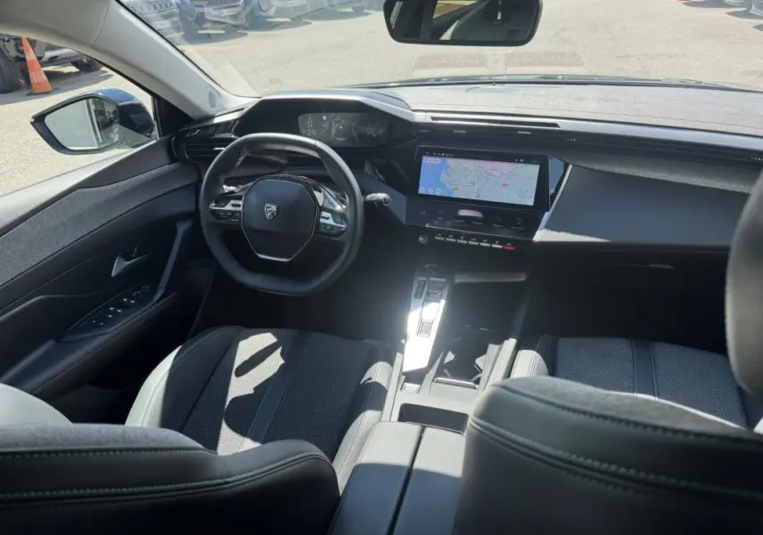 Vue intérieure avant de la Peugeot 308 Hybrid noire 2024, avec volant compact et écran tactile central affichant la navigation.