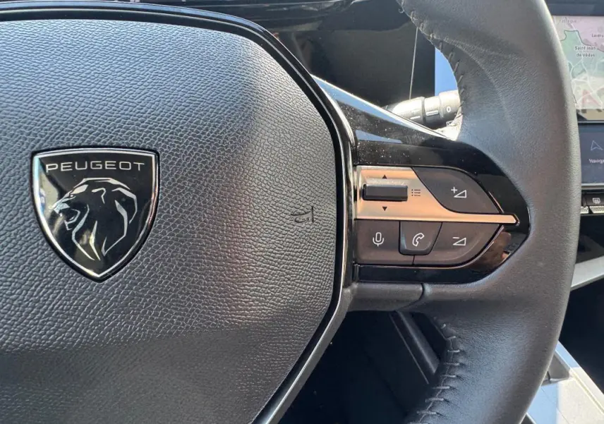Gros plan sur le volant noir de la Peugeot 308 Hybrid 136 e-DCS6 Allure avec commandes intégrées côté droit.