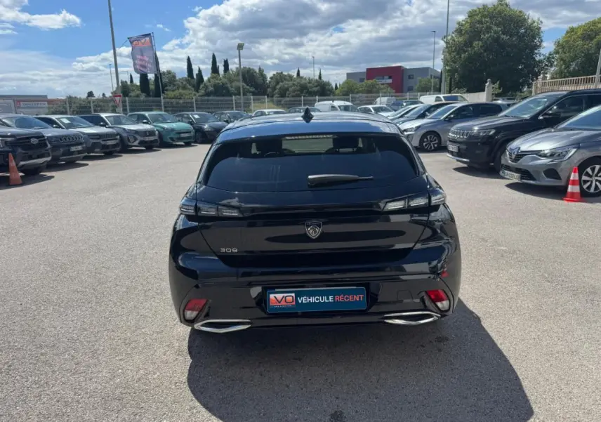Vue arrière d'une Peugeot 308 Hybrid noire 2024 avec feux LED et double sortie d'échappement chromée sur parking.