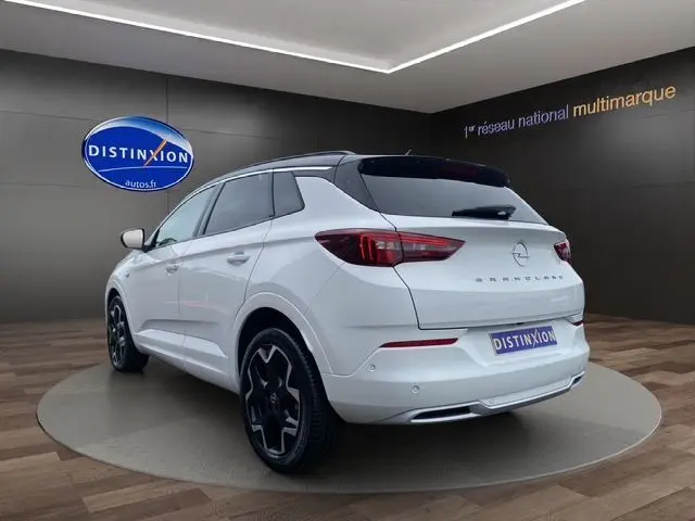 Vue 3/4 arrière droite d'un Opel Grandland blanc Arktis avec toit noir et jantes alliage noires dans un showroom.