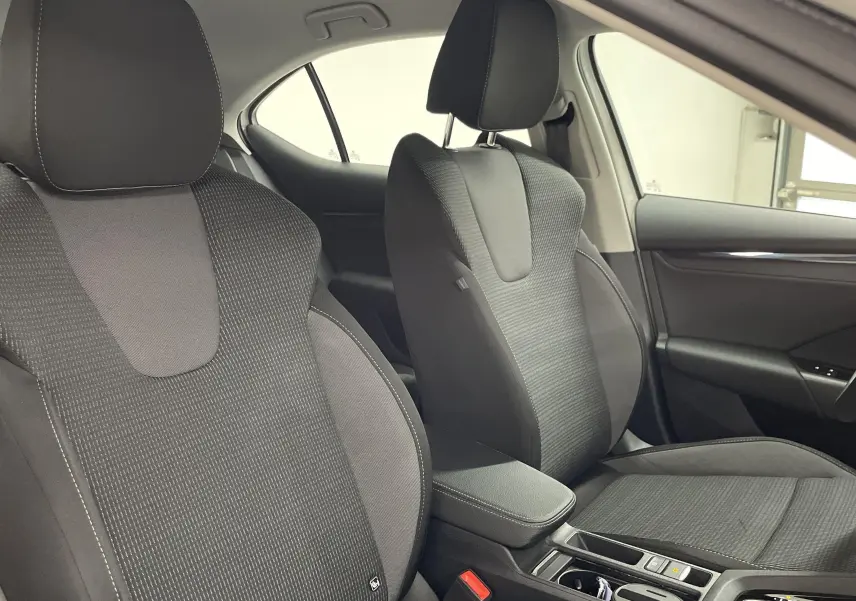 Vue intérieure côté conducteur de la SKODA OCTAVIA 2024, sièges tissu gris foncé avec accoudoir central et garnitures noires.
