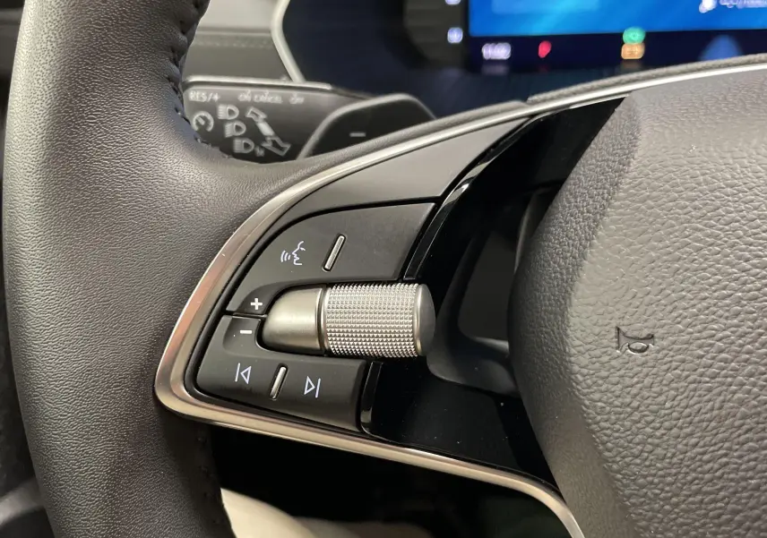 Gros plan sur les commandes gauche du volant noir d'une Skoda Octavia 2024, avec molette et boutons de contrôle audio.