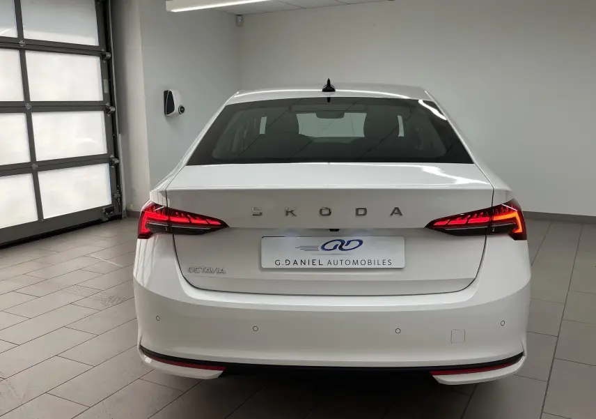 Vue arrière d'une Skoda Octavia blanche Candy 2024 avec feux allumés dans un garage lumineux.